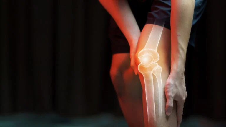 Person experiencing knee joint pain in cold weather while holding their knee for support